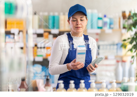 In sales area of pharmacy, builder woman examines packaging of cream 129032019