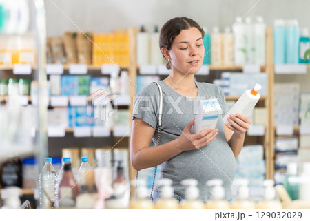 Pregnant woman customer holding and selecting cream or skin care product in drugstore 129032029