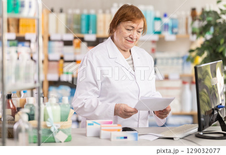 Professional elderly female pharmacist searches for information about medicines on Internet 129032077