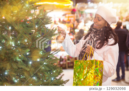 Smiling latin-american woman choosing fir tree for New Year celebration at street fair Smiling latin-american woman choosing fir tree for New Year celebration at street fair 129032098