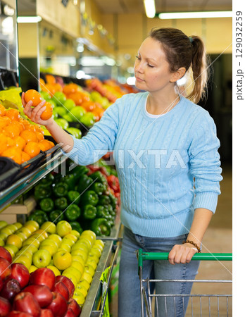 Portrait of calm adult European woman buying local citrus tangerines during shopping in supermarket 129032259