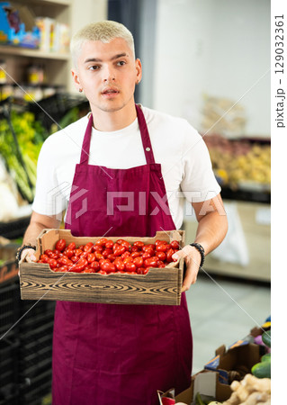 Man salesperson carries cherry tomatoes from warehouse to sales area in shop 129032361