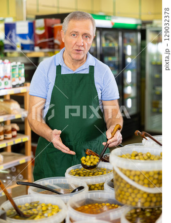 Elderly salesman showing olives in grocery store 129032378