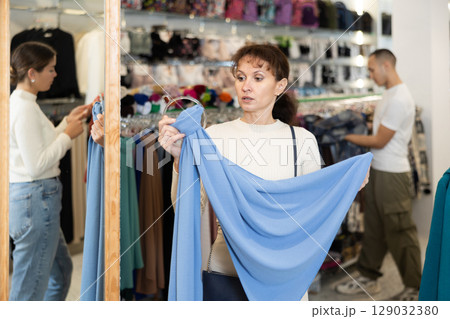 Middle-aged woman choosing thin scarf in clothing store 129032380
