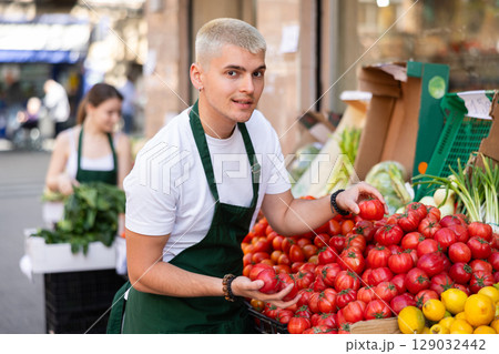 Guy shop seller puts tomatoes on display case 129032442