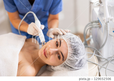 Young woman cosmetologist doing microcurrent procedure to young woman Young woman cosmetologist doing microcurrent procedure to young woman 129032506