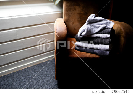 Stack of folded towels on brown armchair in cozy room with soft lighting 129032540