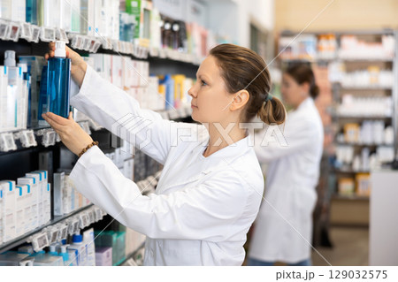 In chemist s shop, woman consultant designs showcase with beauty care cosmetics In chemist s shop, woman consultant designs showcase with beauty care cosmetics 129032575