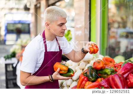 Young guy seller puts peppers in vegetable shop Young guy seller puts peppers in vegetable shop 129032581
