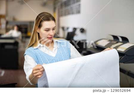 Printing establishment worker examining large piece of paper 129032694