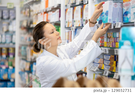 Young female pharmacist arranges product in pharmacy 129032731