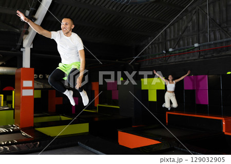 Joyful young man jumping on trampolines in colorful amusement park Joyful young man jumping on trampolines in colorful amusement park 129032905