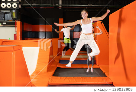 Happy girl bouncing on trampoline in indoor amusement park Happy girl bouncing on trampoline in indoor amusement park 129032909