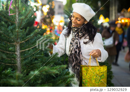 Positive woman choosing New Year's tree in christmas street fair Positive woman choosing New Year's tree in christmas street fair 129032929