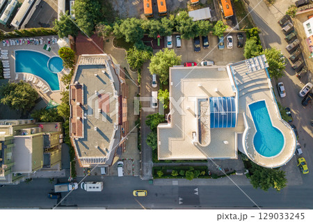 Top down aerial view of hotels roofs, streets with parked cars and swimming pools with blue water in resort city near the sea Top down aerial view of hotels roofs, streets with parked cars and swimming pools with blue water in resort city near the sea 129033245