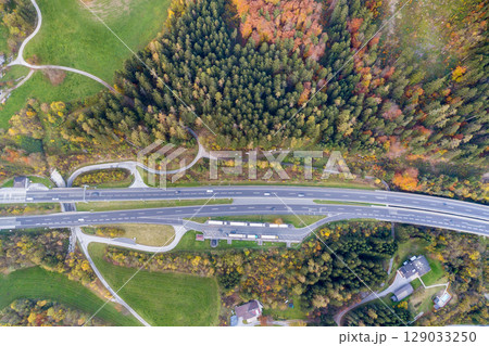 Top dawn aerial view of freeway speed road between yellow autumn forest trees in rural area. 129033250