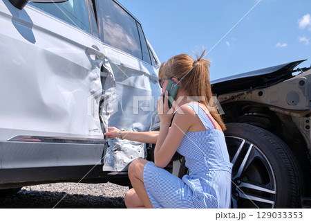 Stressed woman driver talking on mobile phone on street side calling for emergency service after car accident. Road safety and insurance concept Stressed woman driver talking on mobile phone on street side calling for emergency service after car accident. Road safety and insurance concept 129033353