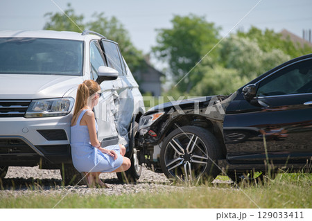 Sad female driver sitting on street side shocked after car accident. Road safety and vehicle insurance concept Sad female driver sitting on street side shocked after car accident. Road safety and vehicle insurance concept 129033411