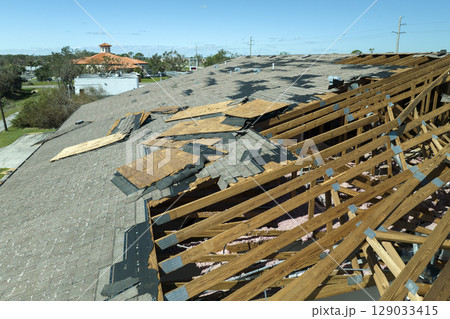 Ruined rooftop in need of repair. Wind damaged house roof with missing asphalt shingles after hurricane Ian in Florida 129033415
