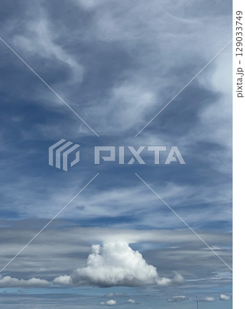 Towering Cumulus Cloud Beneath Swirling Blue and Gray Sky 129033749