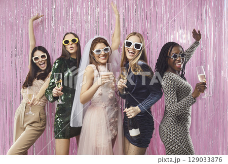 Cheerful diverse stylish women in glamorous dresses celebrating bachelorette party with champagne. 129033876