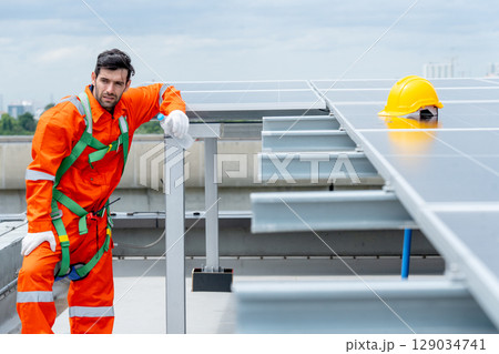 Side view professional technician worker or engineer stand near solarcell panel and relax with action of tired in area of factory or rooftop building. Side view professional technician worker or engineer stand near solarcell panel and relax with action of tired in area of factory or rooftop building. 129034741