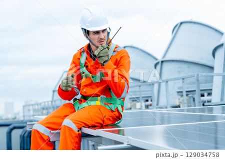 Professional technician worker or engineer use walkie-talkie to discuss with co-worker and sit on solarcell panel during check or maintenance in area of factory or rooftop building. 129034758