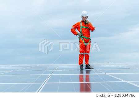 Technician worker or professional engineer stand on solarcell panel and use walkie-talkie during check and maintenance on rooftop of factory building with cloudy sky. Technician worker or professional engineer stand on solarcell panel and use walkie-talkie during check and maintenance on rooftop of factory building with cloudy sky. 129034766