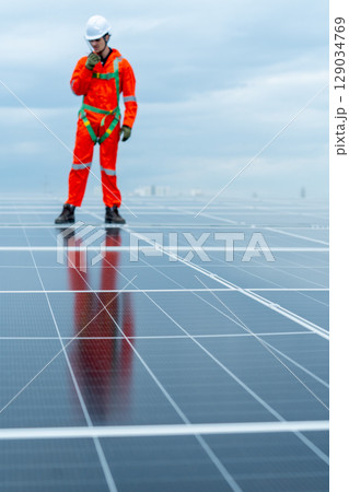 Vertical image with main focus on solar cell panel with technician worker or professional engineer stand and use walkie-talkie during check and maintenance. Vertical image with main focus on solar cell panel with technician worker or professional engineer stand and use walkie-talkie during check and maintenance. 129034769