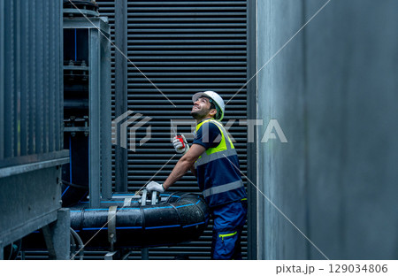 Medium shot of engineer or technician worker hold  walkie talkie and stand with looking and maintenance during work with steel pipe system of factory building. 129034806