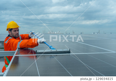 Front view profession engineer or technician worker use cleaning brush to clean solarcell panel in area of rooftop of building. 129034815