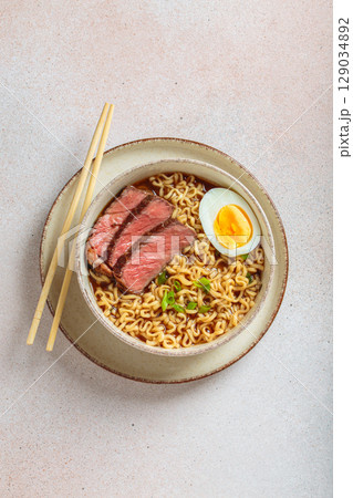Ramen or asian style noodles soup with beef, egg and green onions in bowl on light beige background top view Ramen or asian style noodles soup with beef, egg and green onions in bowl on light beige background top view 129034892