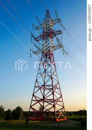 Red and White High Voltage Power Transmission Tower Against Clear Blue Evening Sky 129034907