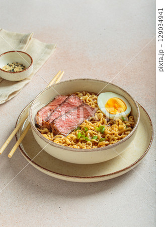 Ramen or asian style noodles soup with beef, egg and green onions in bowl on light beige background Ramen or asian style noodles soup with beef, egg and green onions in bowl on light beige background 129034941