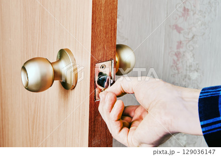 Locksmith inserts screw into mortise hole of latch plate on wooden door to secure plate during hardware installation process. 129036147