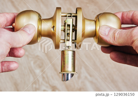 Door lockset components held by hands during assembly showing latch mechanism and alignment of parts before door knob installation. 129036150