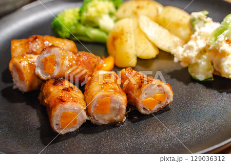 にんじんを巻いた豚肉の肉巻きと副菜が並ぶ夕食プレート にんじんを巻いた豚肉の肉巻きと副菜が並ぶ夕食プレート 129036312