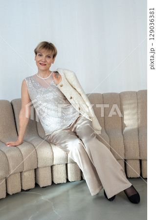 Smiling woman sitting on sofa in bright sunny room. Looking at camera. Vertical photo. High quality photo 129036381