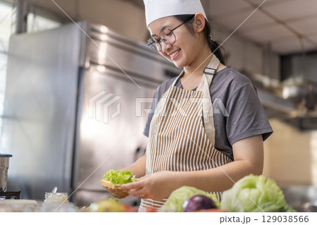 Smiling Young Female Chef Preparing a Sandwich in a Professional Kitchen 129038566