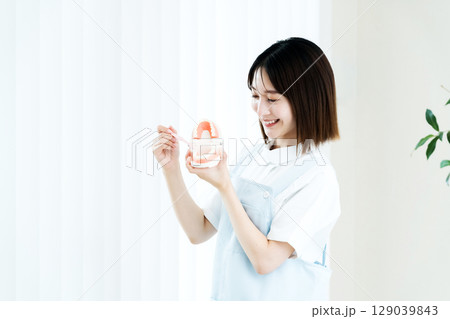 歯ブラシと歯の模型を持つ歯科スタッフの女性 歯ブラシと歯の模型を持つ歯科スタッフの女性 129039843