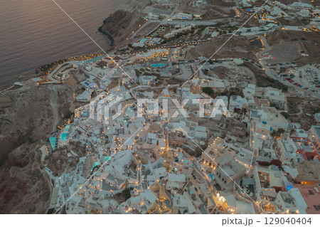 Oia, Santorini, Greece. Evening drone view with warm street lights illuminating the white houses Oia, Santorini, Greece. Evening drone view with warm street lights illuminating the white houses 129040404