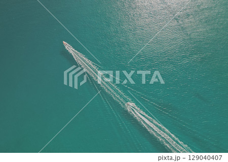 Two boats sailing one after another across crystal clear sea water, drone photo with white trails 129040407