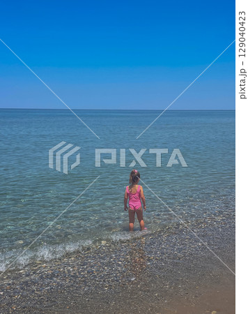 Little 6-year-old girl in a pink swimsuit entering the clean sea to swim alone Little 6-year-old girl in a pink swimsuit entering the clean sea to swim alone 129040423