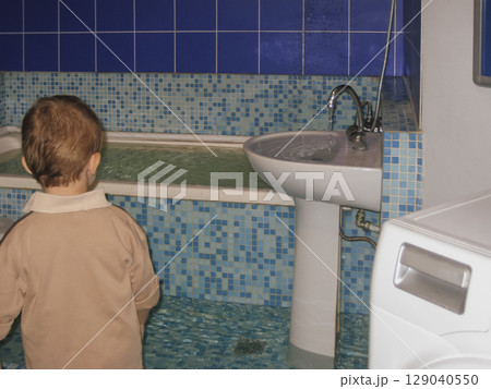 Child watching water overflow from bathtub and sink filling the room Child watching water overflow from bathtub and sink filling the room 129040550