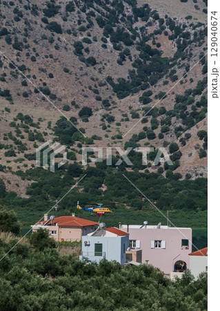 Firefighting helicopter flying low over residential houses near a lake to collect water Firefighting helicopter flying low over residential houses near a lake to collect water 129040674