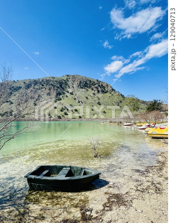 Peaceful Lake Kournas, view of a dry bush, small boat, and tourist pedal boat rental point 129040713