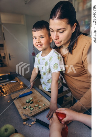 Mother and son preparing fresh vegetables in the kitchen together. The boy smiles while helping cut cucumbers, enjoying quality family time and healthy cooking Mother and son preparing fresh vegetables in the kitchen together. The boy smiles while helping cut cucumbers, enjoying quality family time and healthy cooking 129040796