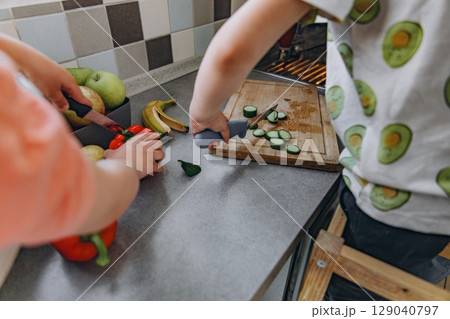 Children prepare vegetables together in a bright kitchen, cutting cucumbers and enjoying family time. Learning, sharing, and healthy eating in a cheerful home environment Children prepare vegetables together in a bright kitchen, cutting cucumbers and enjoying family time. Learning, sharing, and healthy eating in a cheerful home environment 129040797
