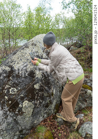 A woman photographs a moss-covered boulder in a lush northern forest using her smartphone 129041524