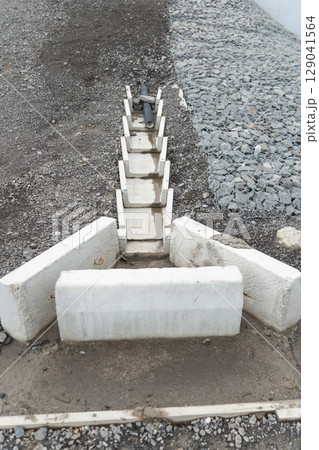 Concrete drainage channel with embedded plastic pipe for stormwater management, set against gravel and gabion-covered slope 129041564